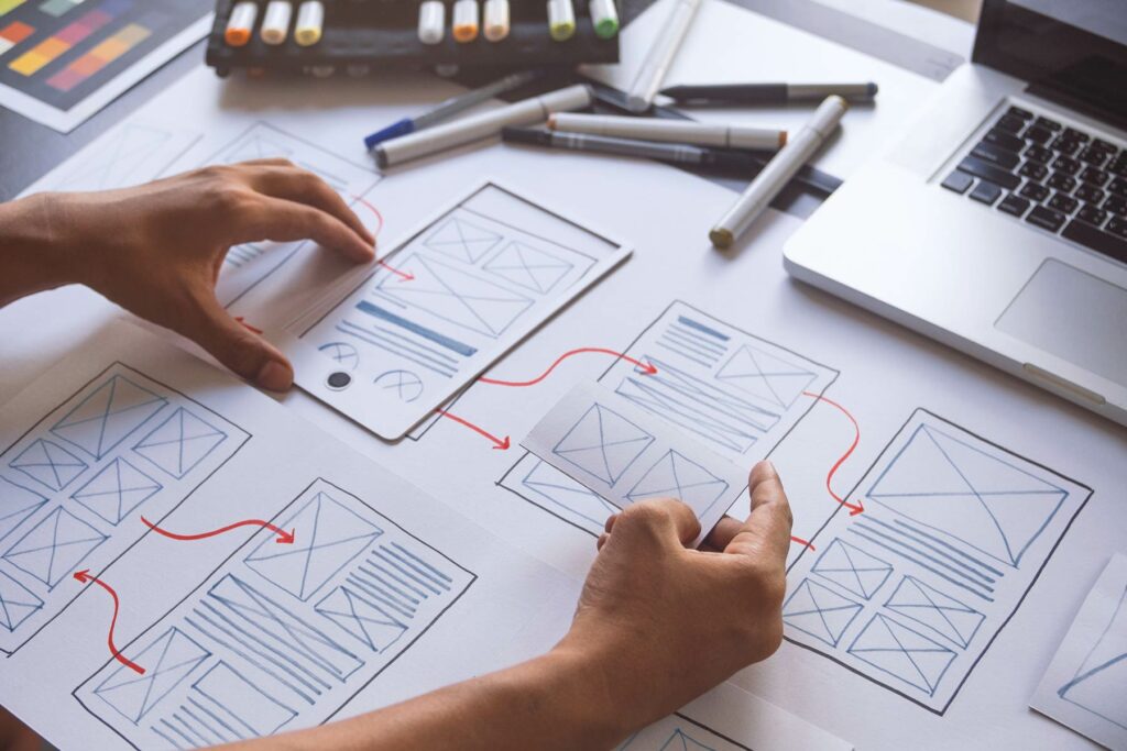 Zwei Hände die auf einem Schreibtisch eine User-Experience auf Papier entwickeln.